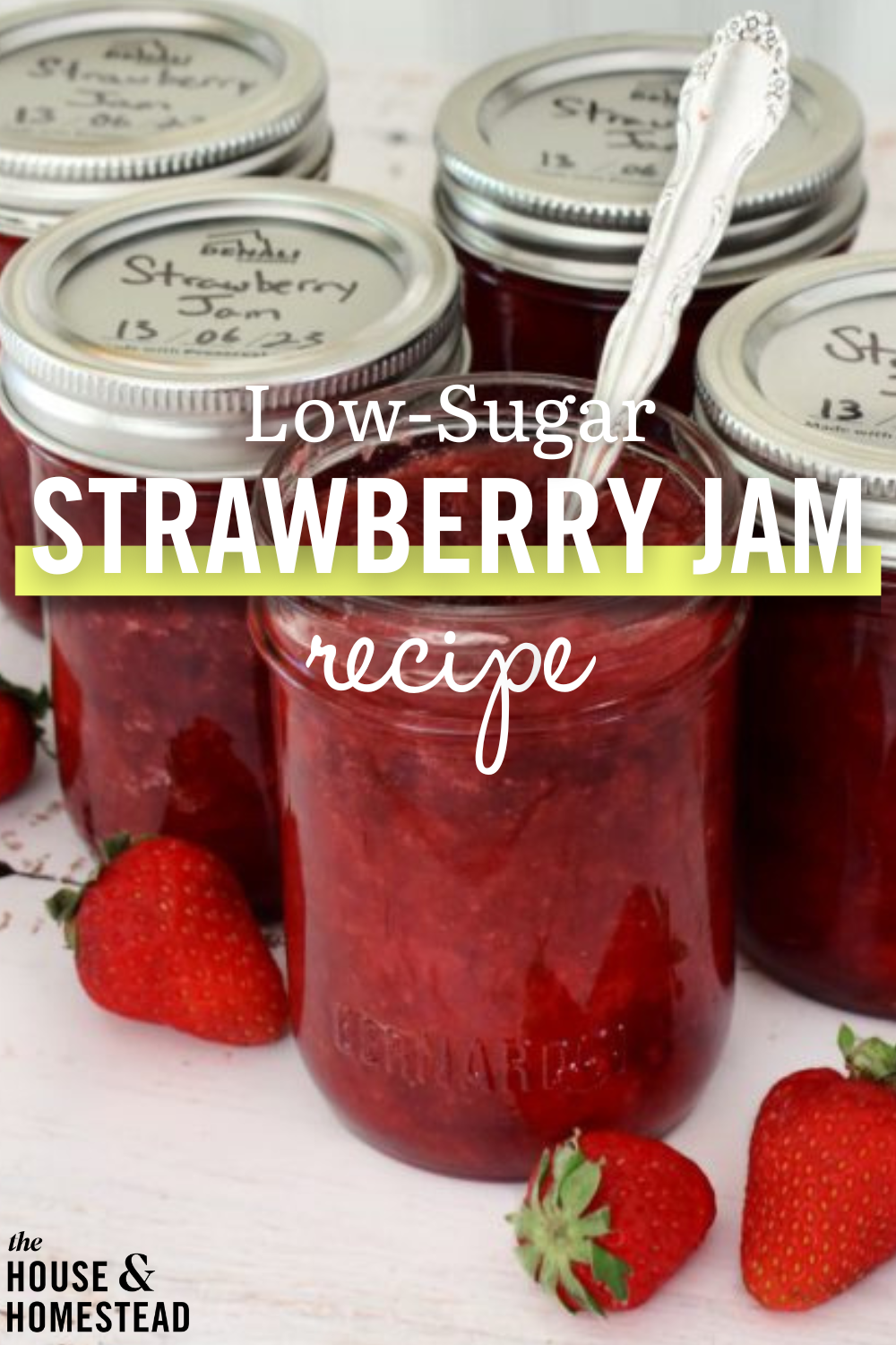 Mason jars filled with red strawberry jam, topped with metal lids, and a spoon inside one jar. Fresh strawberries are scattered around. Text overlay reads "Low-Sugar Strawberry Jam Recipe."