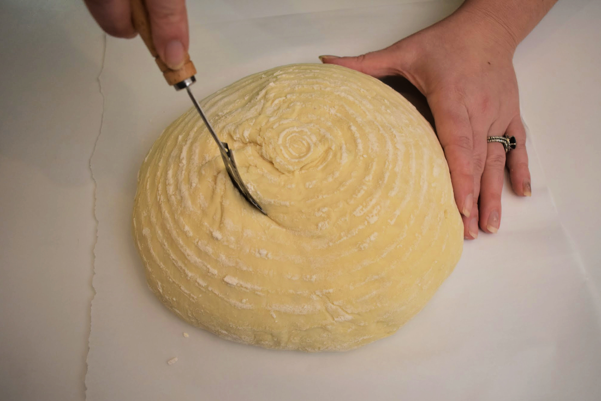 Hands scoring sourdough with a lame.