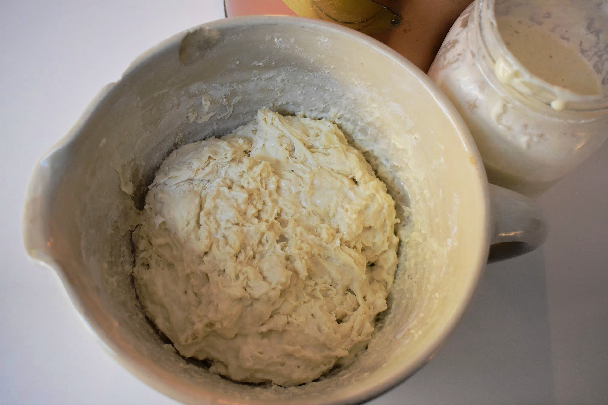 Shaggy sourdough dough in a mixing bowl beside a sourdough starter and flour canister.