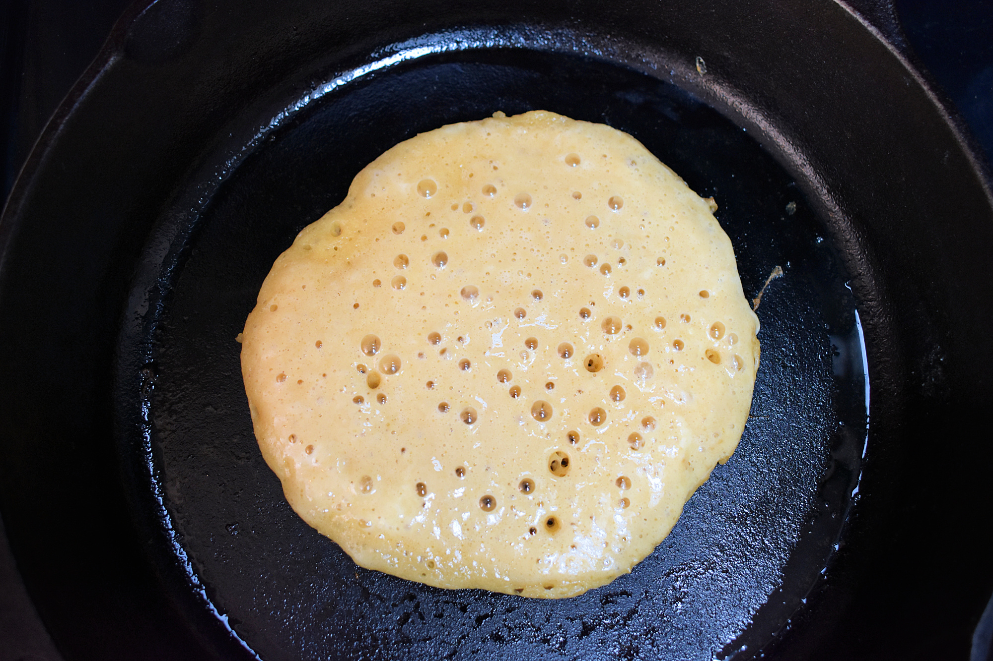 Bubbly pancake batter cooking in a cast iron skillet