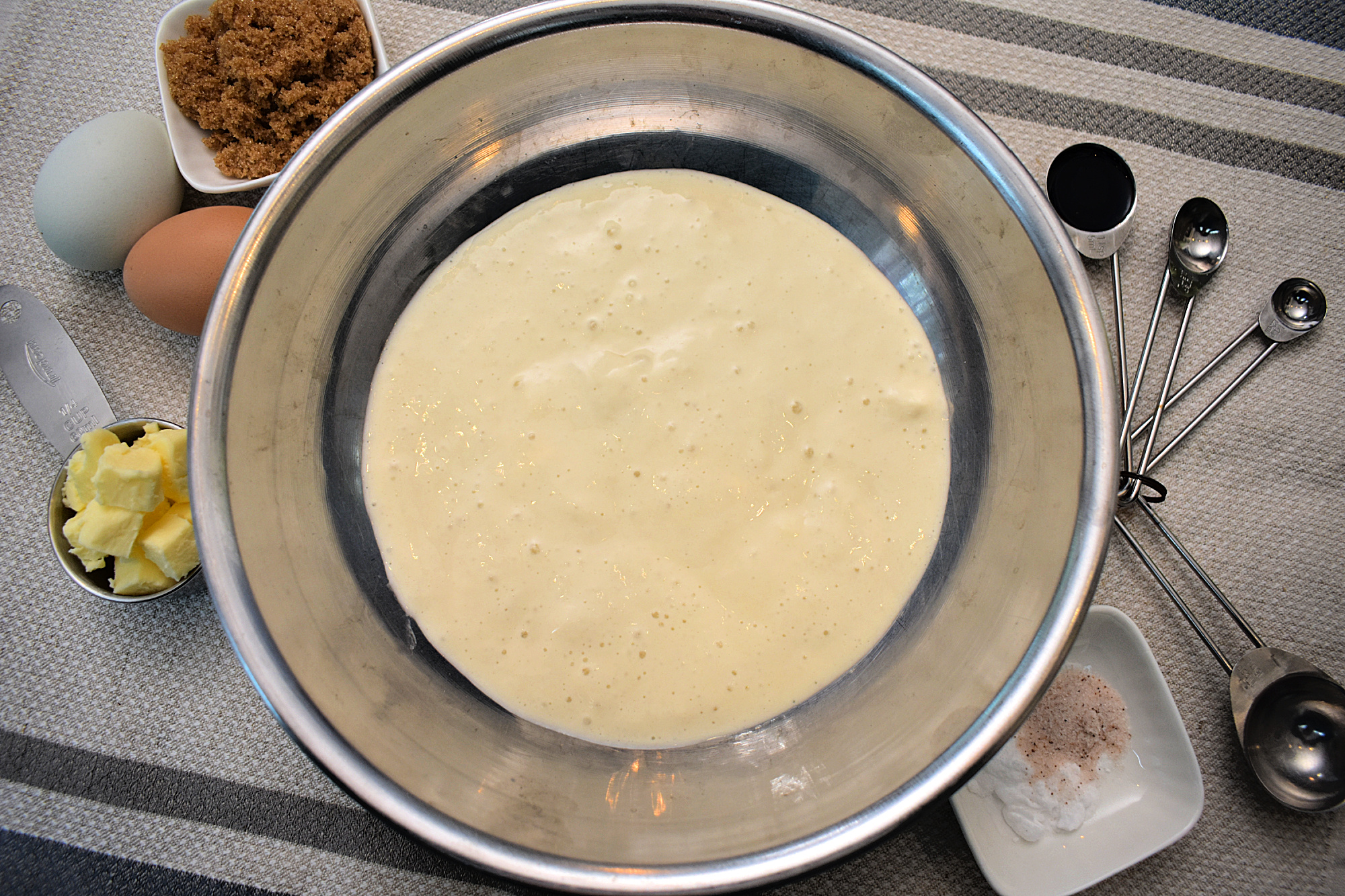 A top-down view of sourdough discard pancake batter. Beside sits brown sugar, fresh eggs, butter, salt, and measuring spoons