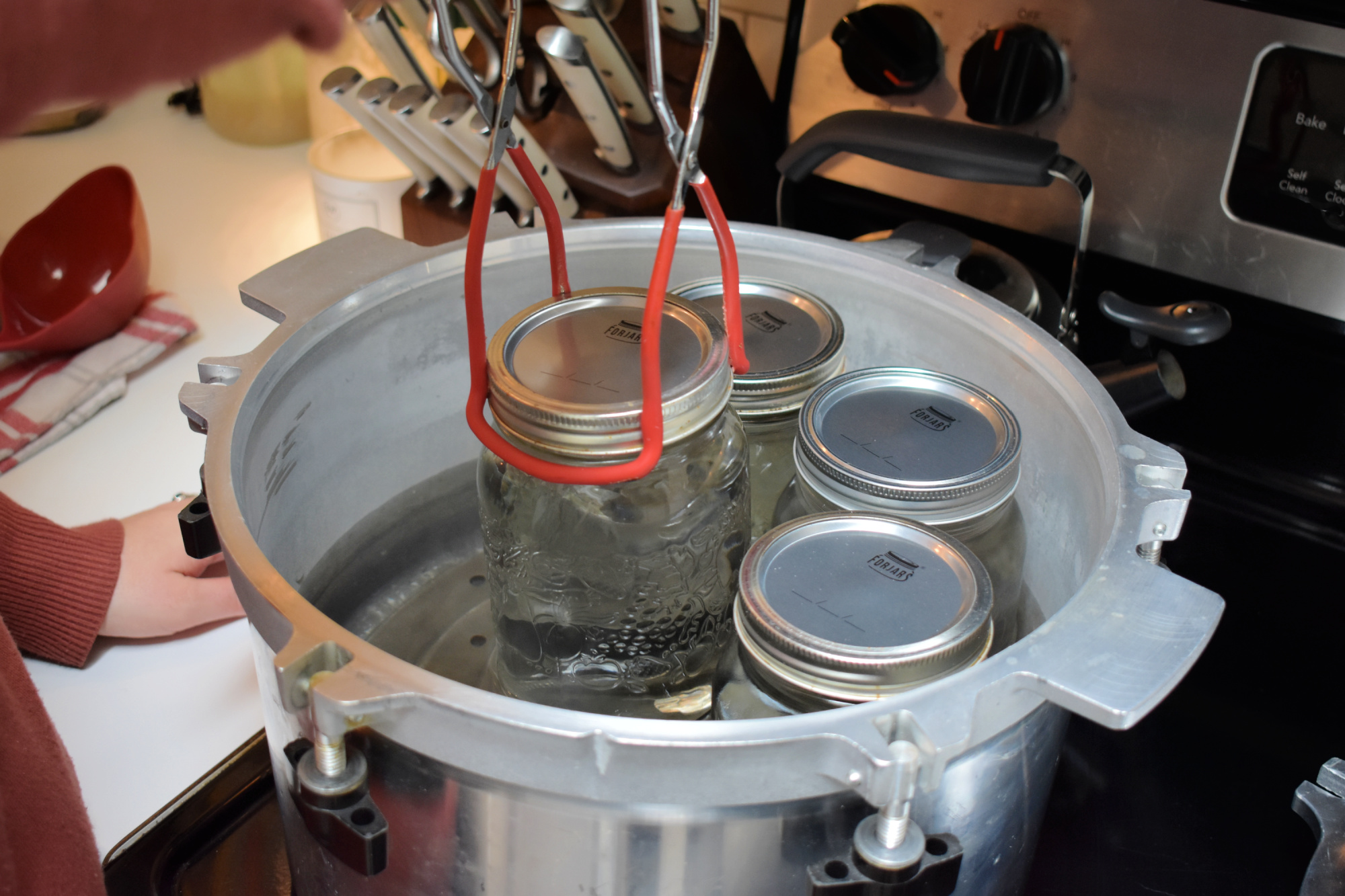 Putting Mason jars full of water into a pressure canner with jar lifters.
