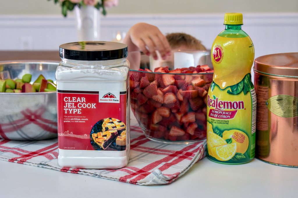 Ingredients for strawberry rhubarb pie filling including sliced strawberries, chopped rhubarb, clear jel, and bottled lemon juice