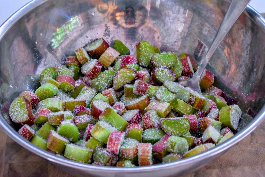 A large metal bowl full of chopped rhubarb covered in white sugar