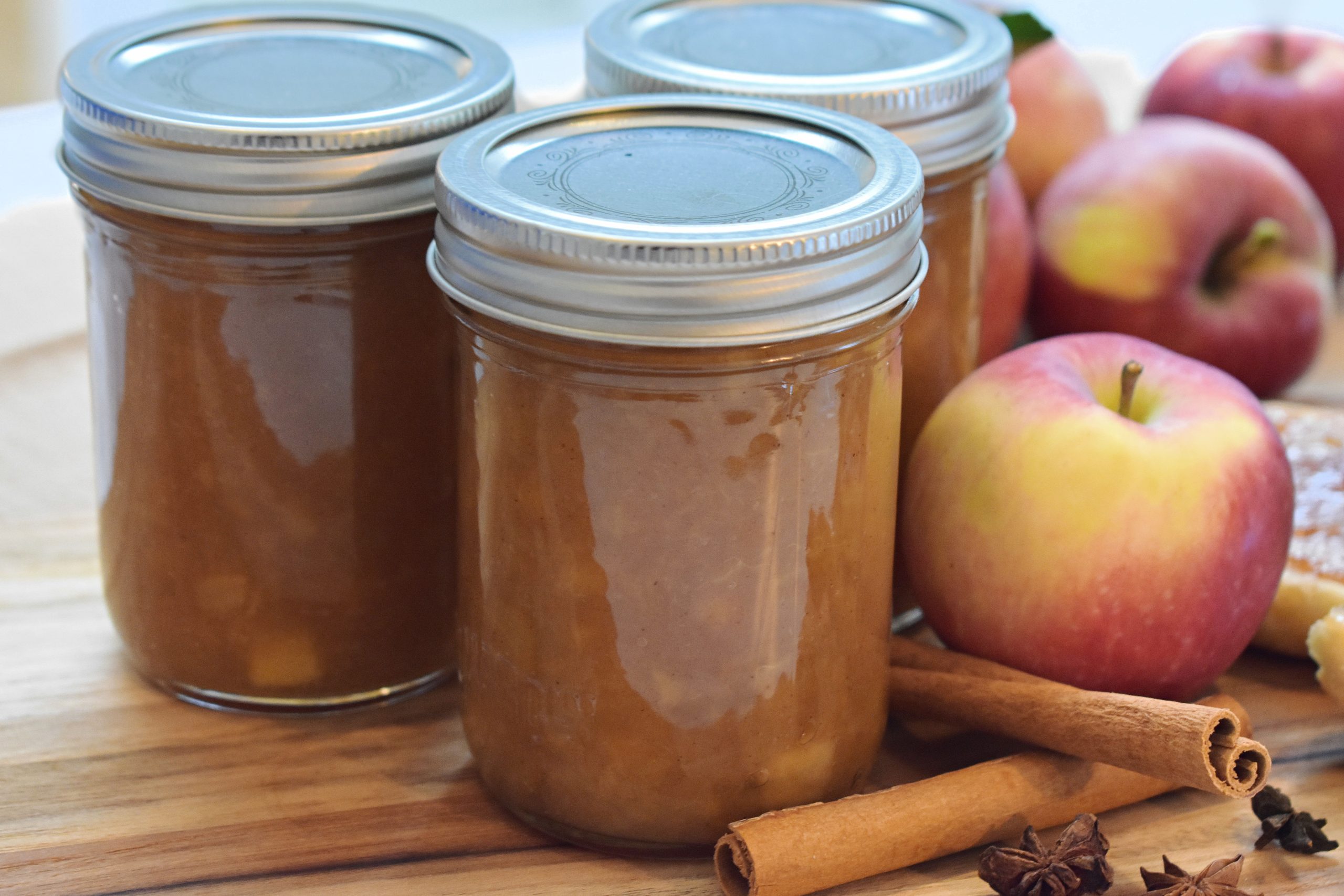Jars of apple pie jam with spices and fresh apples in the background.